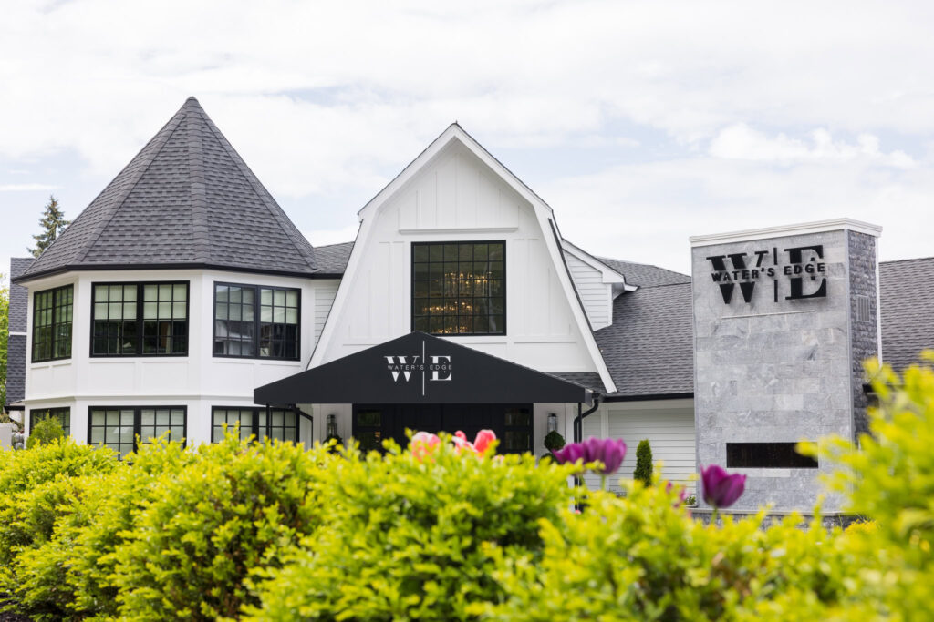 Exterior of Water’s Edge Centerport framed by lush greenery and florals on a sunny day.