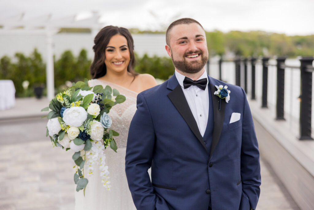 Bride and groom smiling on the terrace at Water’s Edge Centerport with waterfront views behind them.