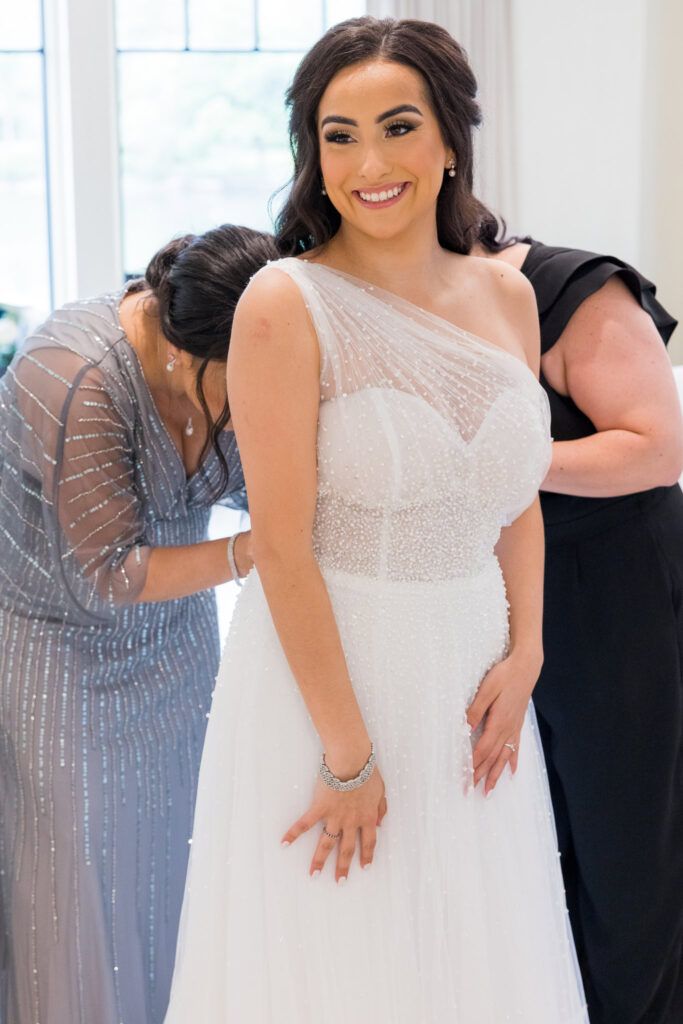 Bride smiles while getting ready with the help of family in a bright suite at Water’s Edge Centerport.