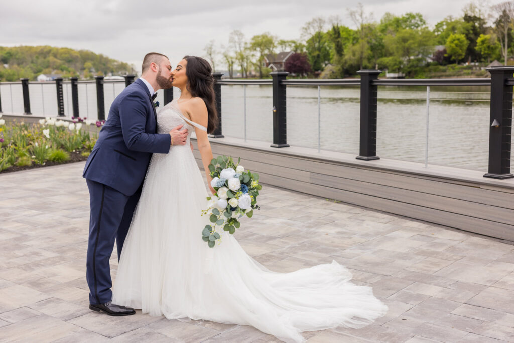 Bride and groom share a kiss beside the water on the terrace at Water’s Edge Centerport.