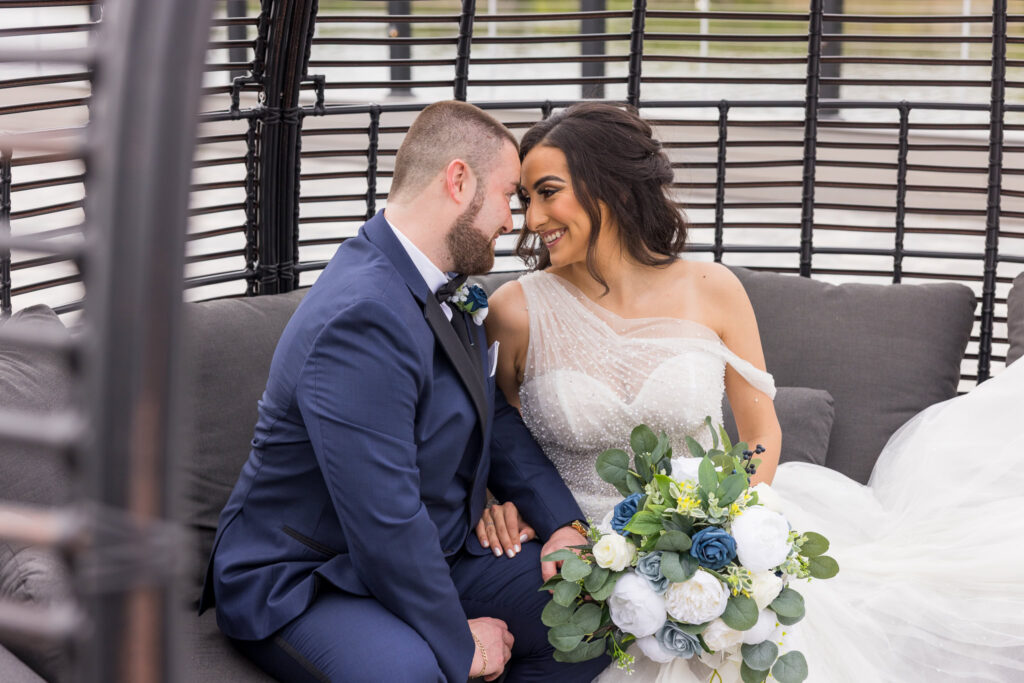 Bride and groom sit close together in a lounge pod, sharing a joyful moment at Water’s Edge Centerport.