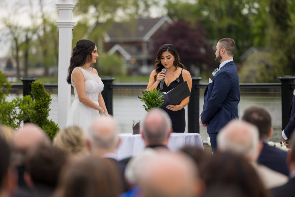 Bride and groom listen as a family member officiates their outdoor wedding ceremony at Water’s Edge Centerport.