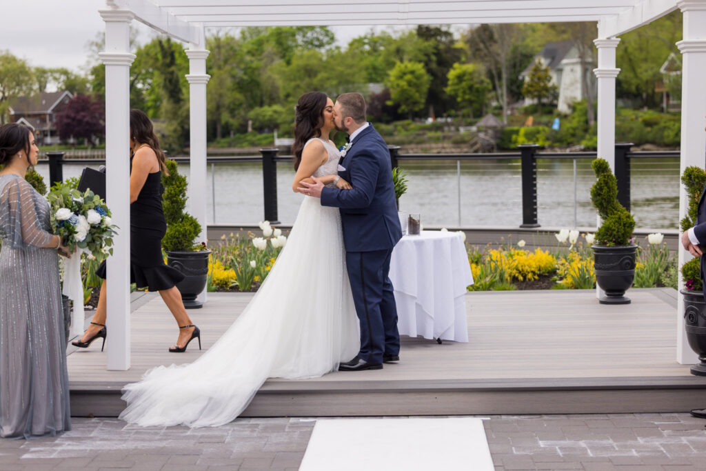 Bride and groom share their first kiss as newlyweds under the pergola at Water’s Edge Centerport.