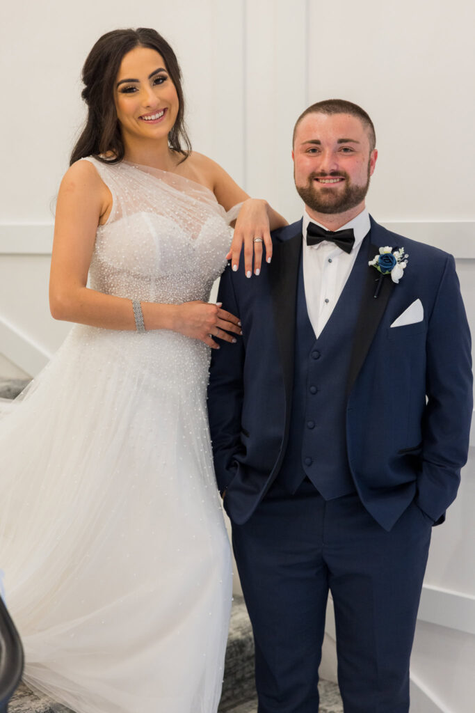  Bride and groom pose confidently on the staircase at Water’s Edge Centerport in elegant wedding attire.