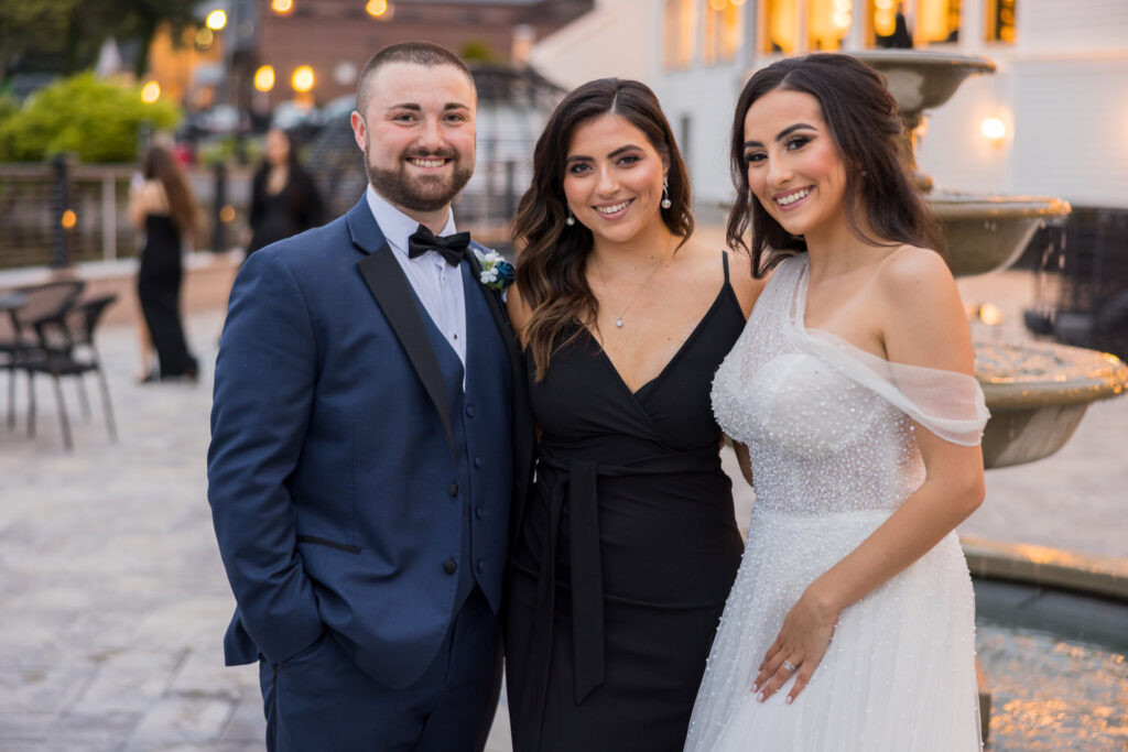 Bride and groom smile with the officiant during cocktail hour at Water’s Edge Centerport.