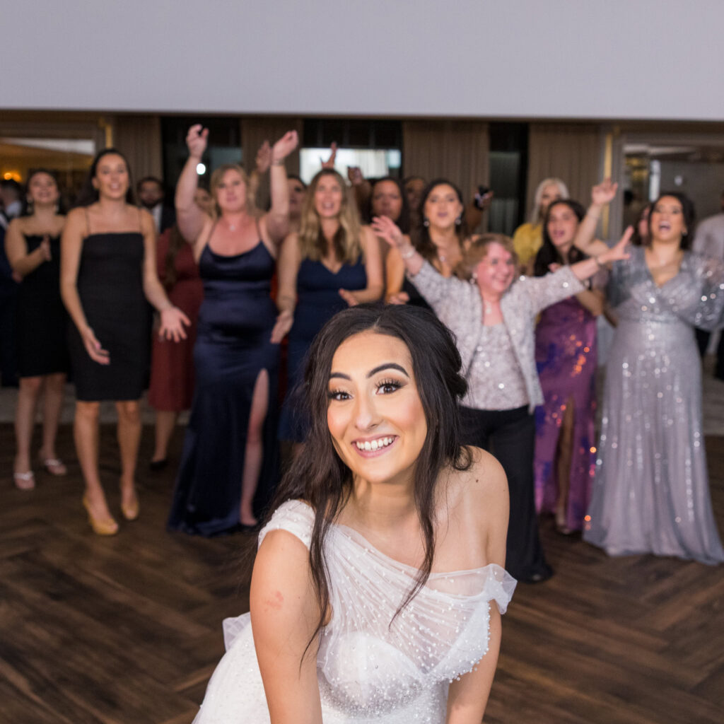 Bride smiles as guests gather behind her for the bouquet toss at Water’s Edge Centerport.