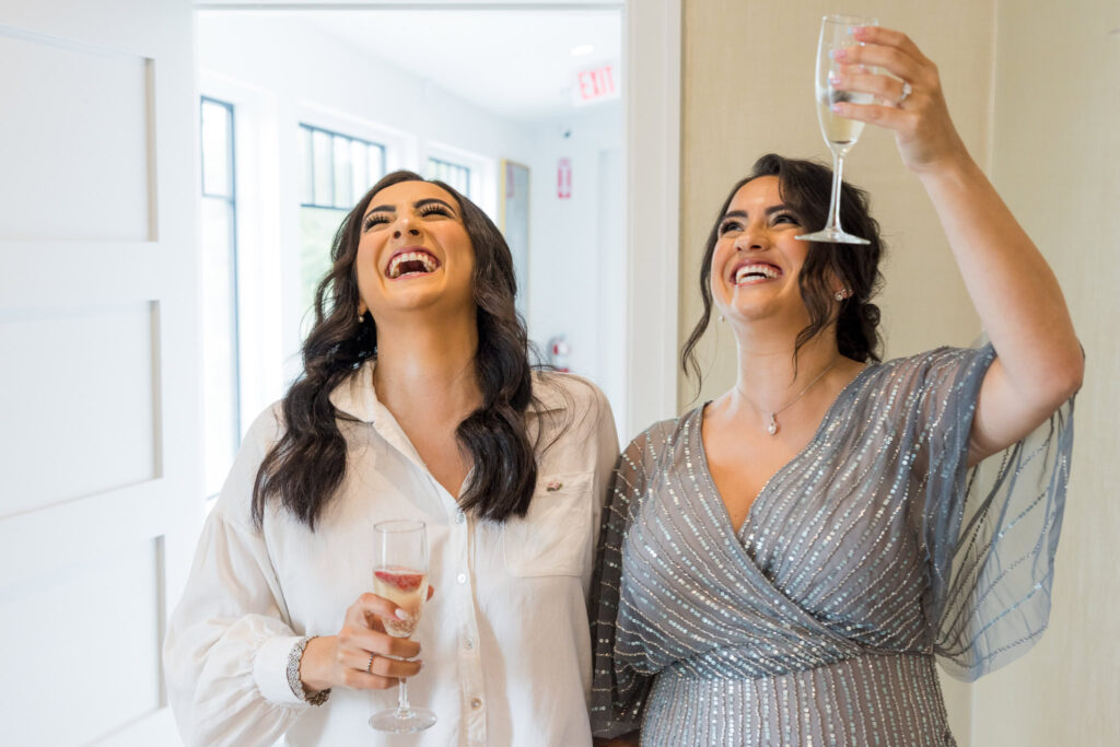 Bride and mother share a joyful toast during wedding morning preparations at Water’s Edge Centerport.