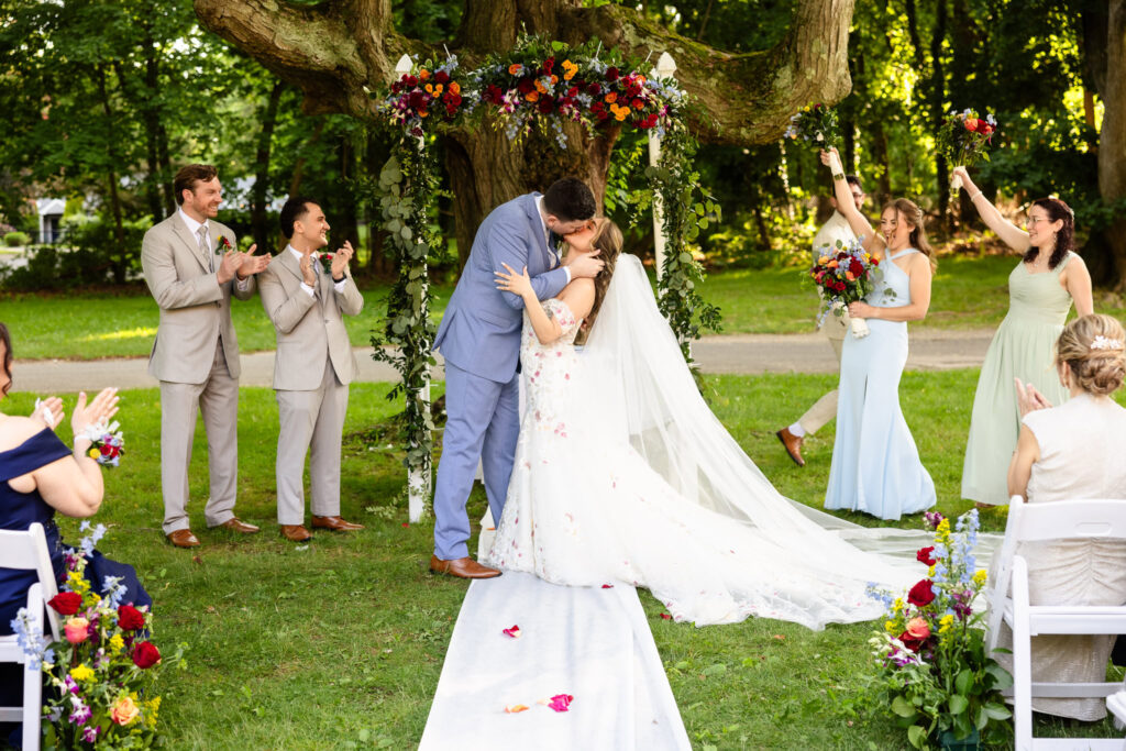 Newlyweds sharing first kiss under floral arch in garden ceremony