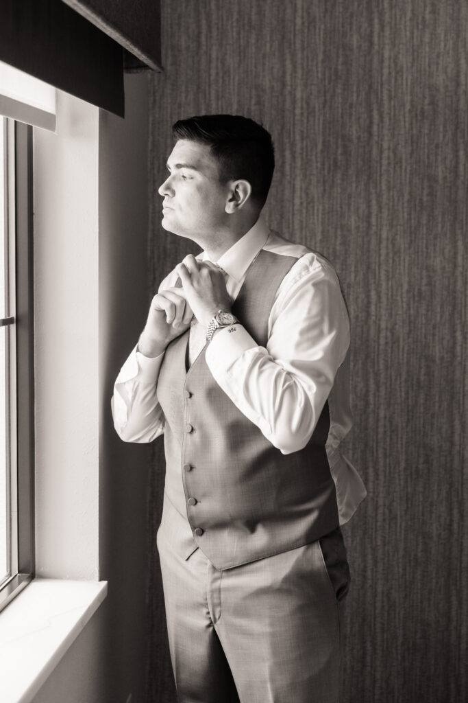 Groom looking out the window with quiet anticipation during wedding morning preparations