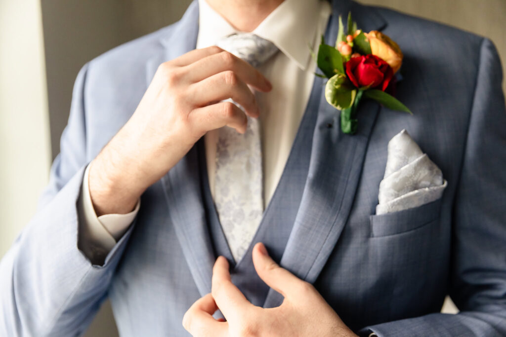Groom adjusting tie with boutonnière before wedding at Coindre Hall