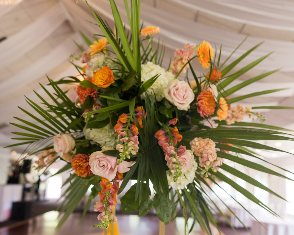 Lush floral centerpiece at Flowerfield, featuring vibrant roses, snapdragons, and tropical greenery beneath soft ceiling draping in the Grand Ballroom.

