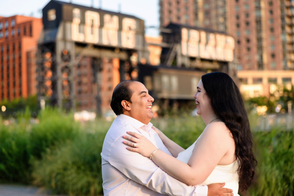 Suzie and Roberto share a joyful embrace in front of the Long Island City sign during their Gantry Plaza engagement session.