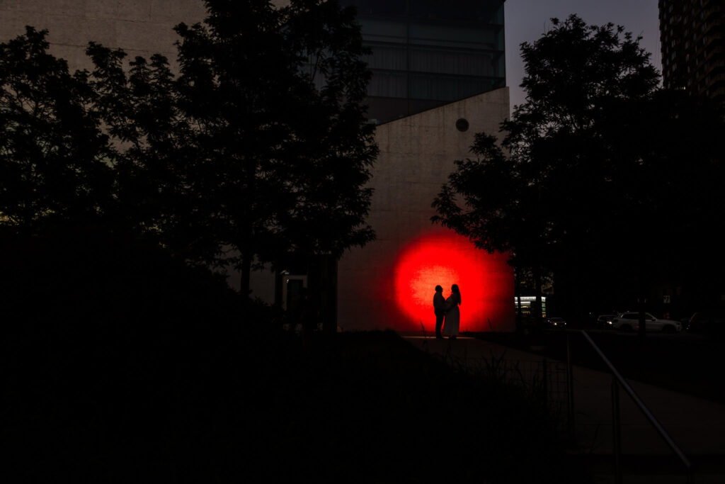 Silhouetted couple framed by a glowing red light during their Gantry Plaza engagement session at dusk.