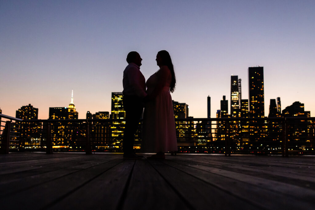 Silhouette of Suzie and Roberto sharing a quiet moment with the Manhattan skyline glowing behind them at sunset.