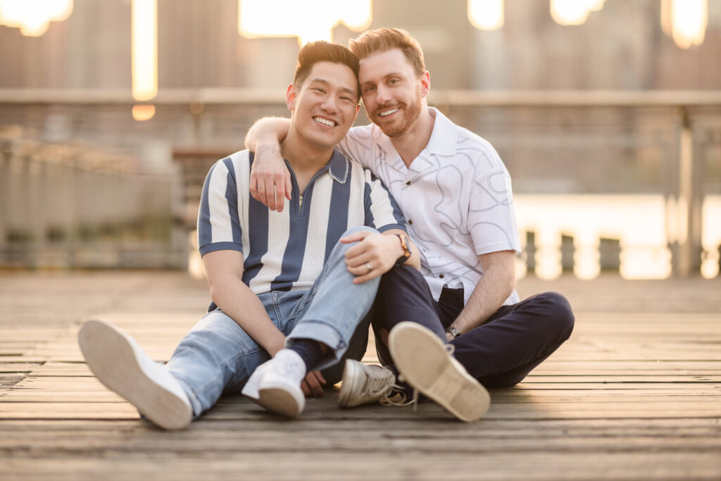 Dave and Peter sit side by side on the boardwalk, leaning in close and laughing together in the soft light of spring.