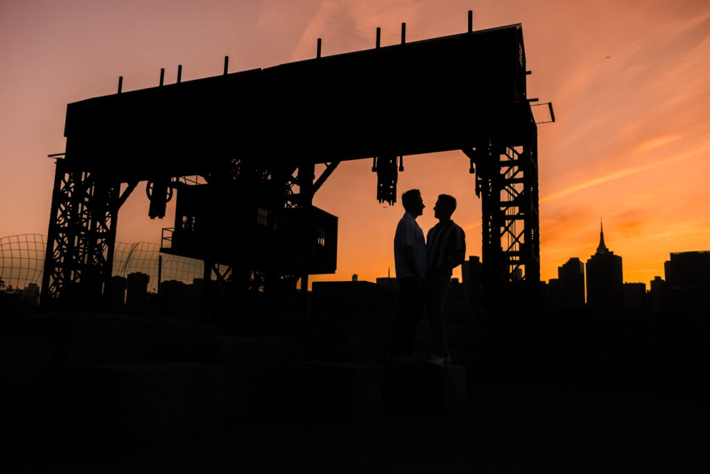 A striking silhouette of Dave and Peter standing beneath the gantries at dusk, framed by dramatic color and quiet intimacy.
