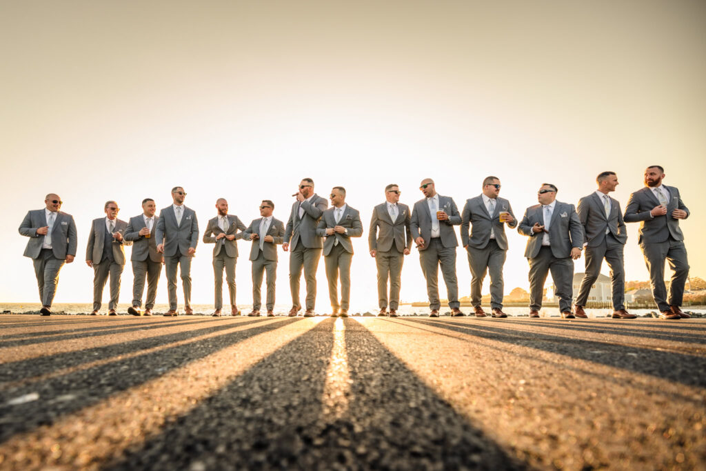 Groomsmen walking in formation down a sunlit path, captured in a dynamic, low-angle shot with golden light.