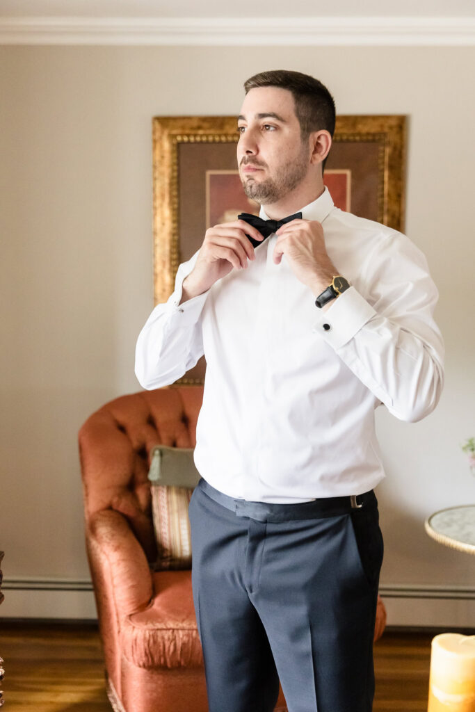 Groom adjusting his black bow tie while getting ready for his wedding at Watermill Caterers in Smithtown.