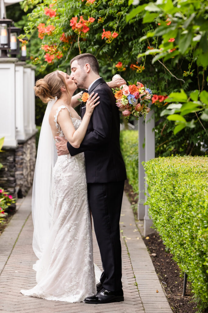 Bride and groom sharing a kiss beneath flowering vines in the garden at Watermill Caterers in Smithtown, New York.