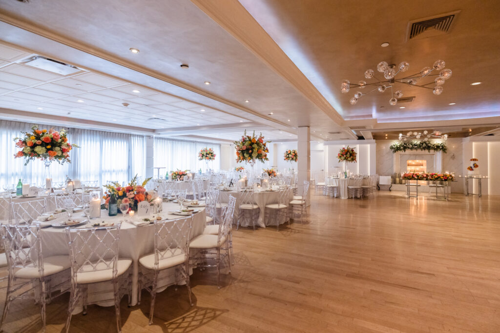 Wide view of the Grand Ballroom at Watermill Caterers showcasing spacious reception seating, modern chandeliers, floral décor, and a fireplace feature on Long Island.