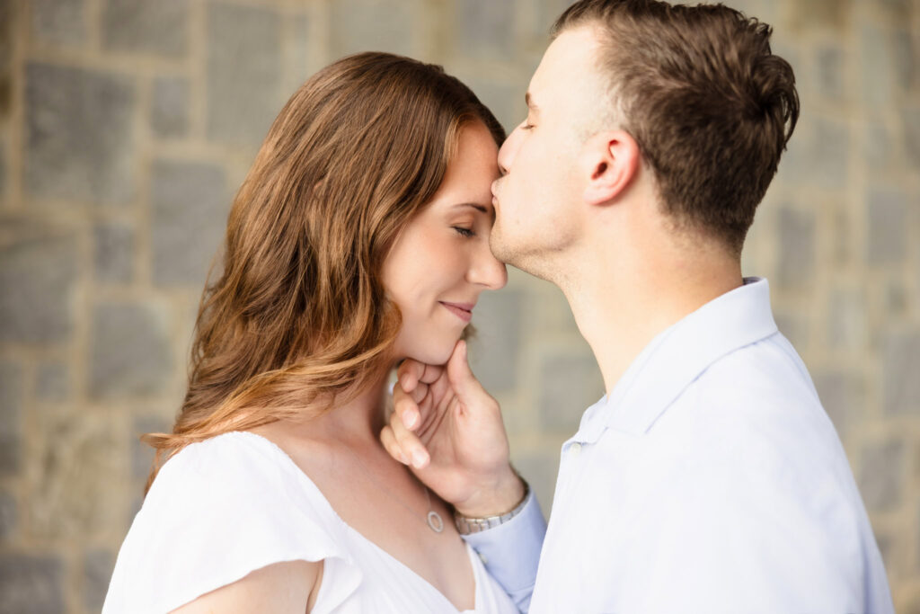 Groom kissing bride’s temple in close embrace