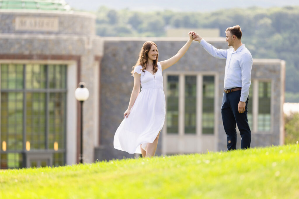 Groom twirling bride on lawn near modern Marist architecture