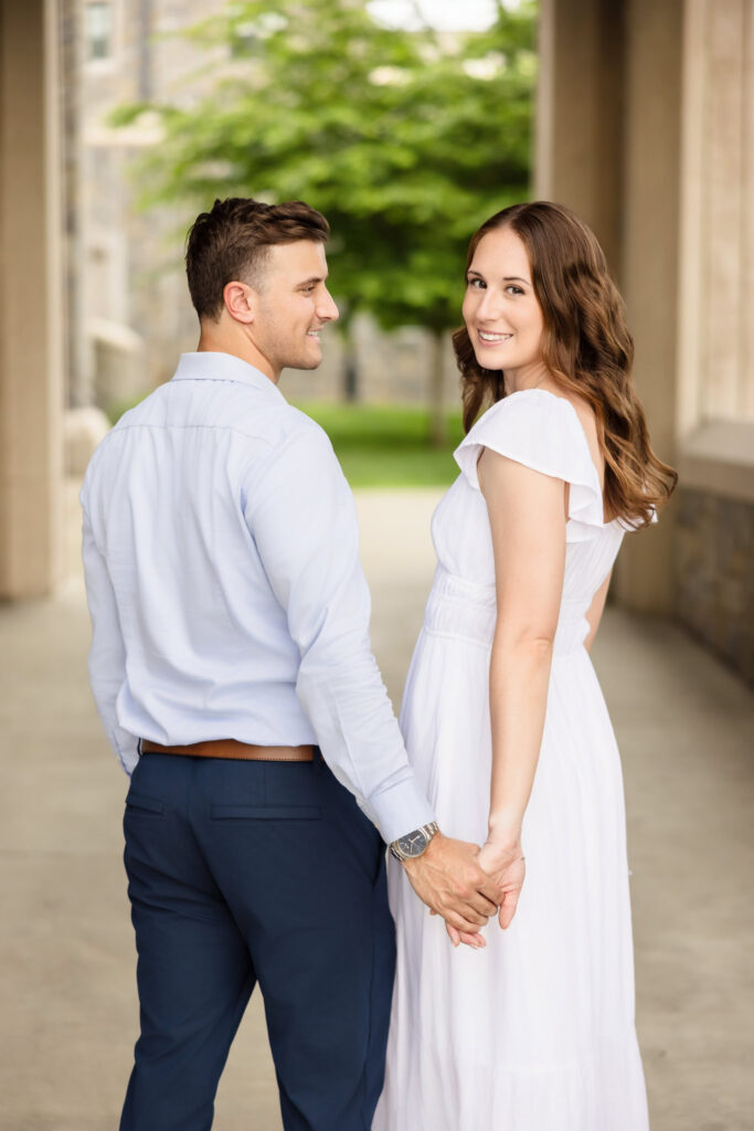 Couple holding hands and smiling near stone archway