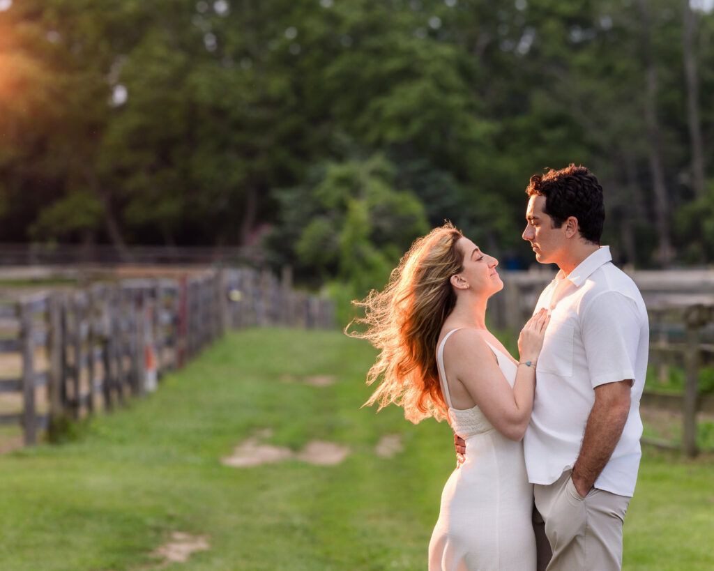 The couple smiling in a sunlit moment surrounded by rustic fencing.