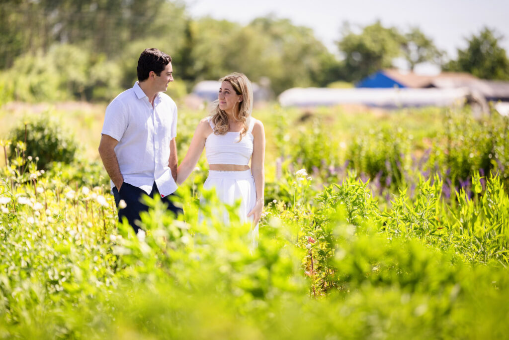 Couple walking hand in hand through sunlit flower fields on the East End of Long Island.