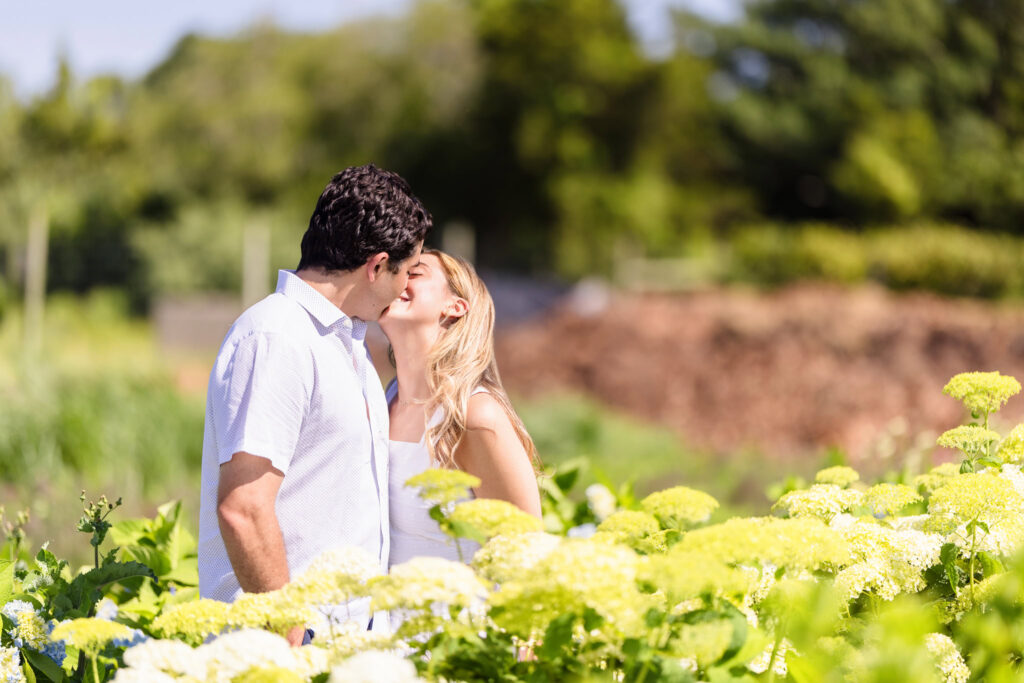 A joyful kiss shared between rows of green foliage and summer blooms.