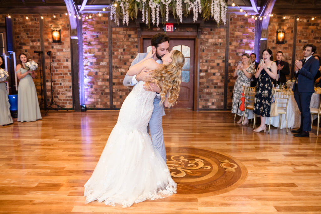Newlyweds share their first dance on the polished wood floor of Riviera’s grand ballroom under warm lighting.