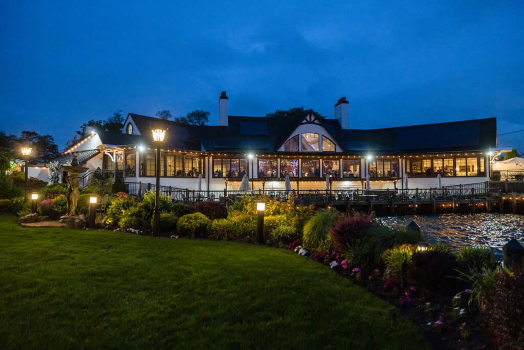 Evening view of Riviera Waterfront Mansion with glowing lights reflecting over the landscaped gardens and bay.