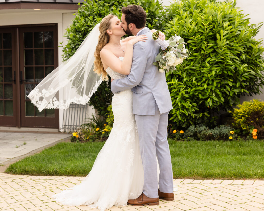Newlyweds embrace and kiss in the garden courtyard of Riviera Waterfront Mansion.