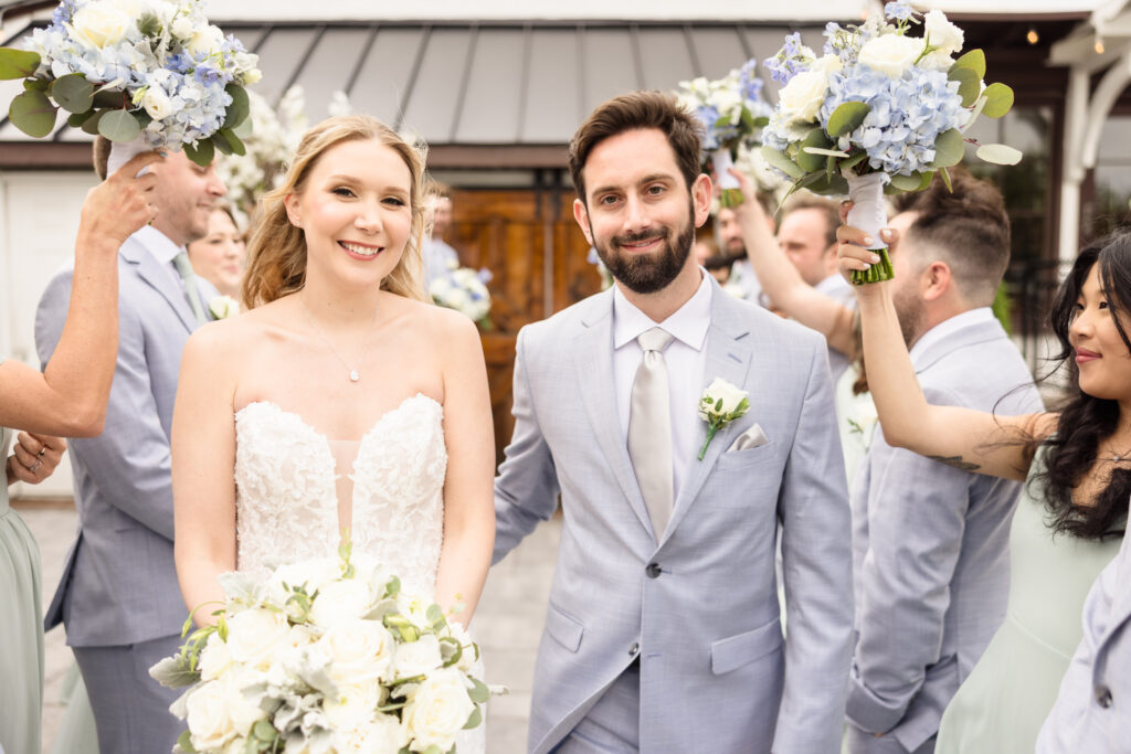 Bride and groom celebrate with their bridal party raising bouquets in front of Riviera Waterfront Mansion.