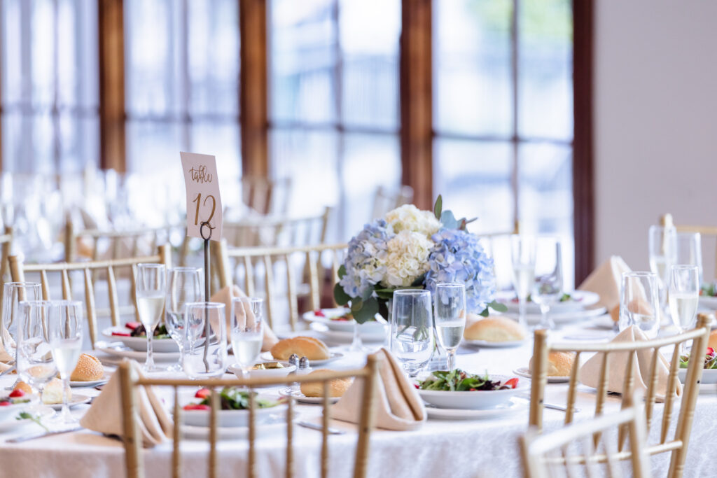 Close-up of a wedding reception table decorated with candles and ivory blooms near the windows of Riviera Waterfront Mansion.