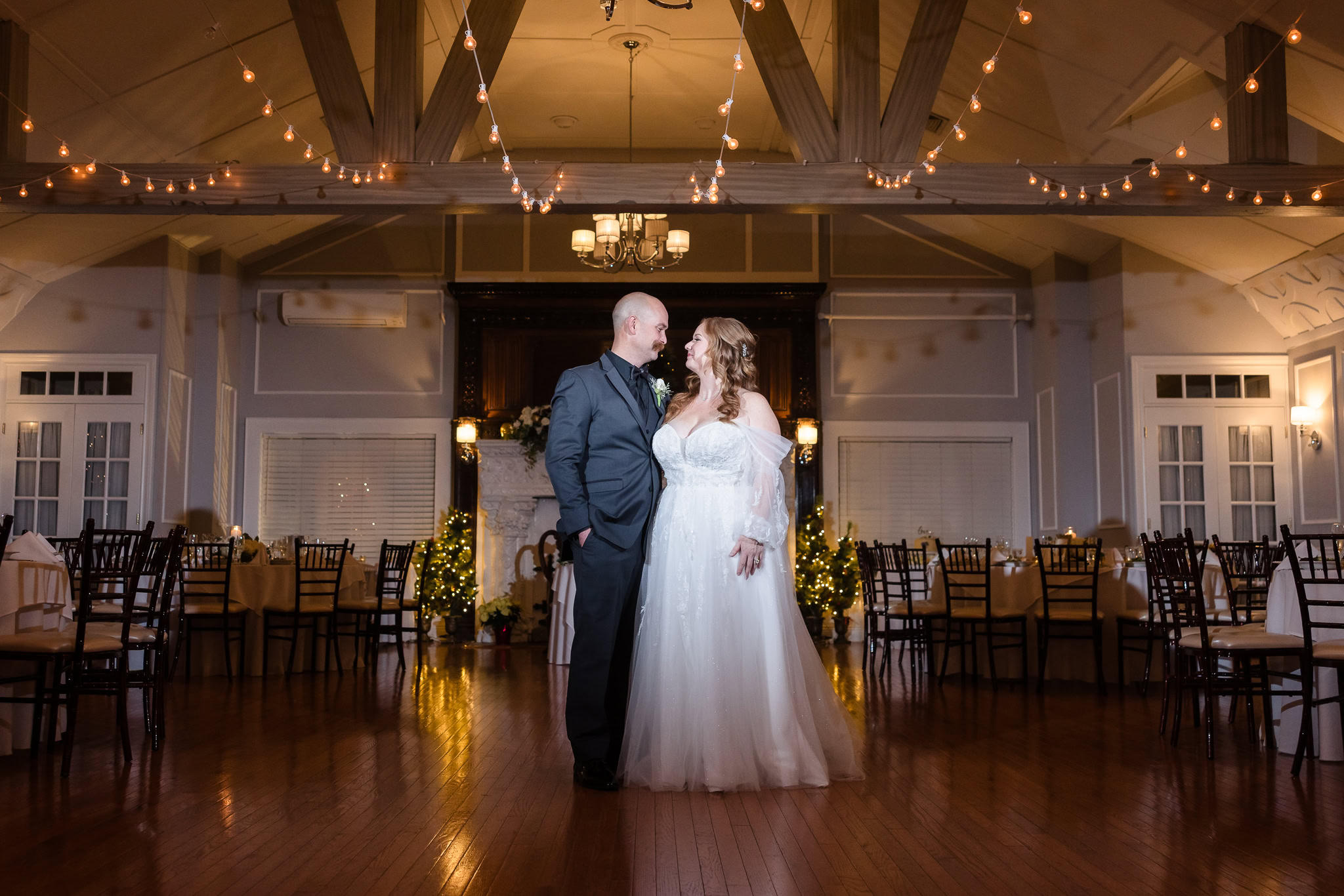 Bride and groom sharing a quiet moment in the softly lit reception room, with bistro lights overhead.