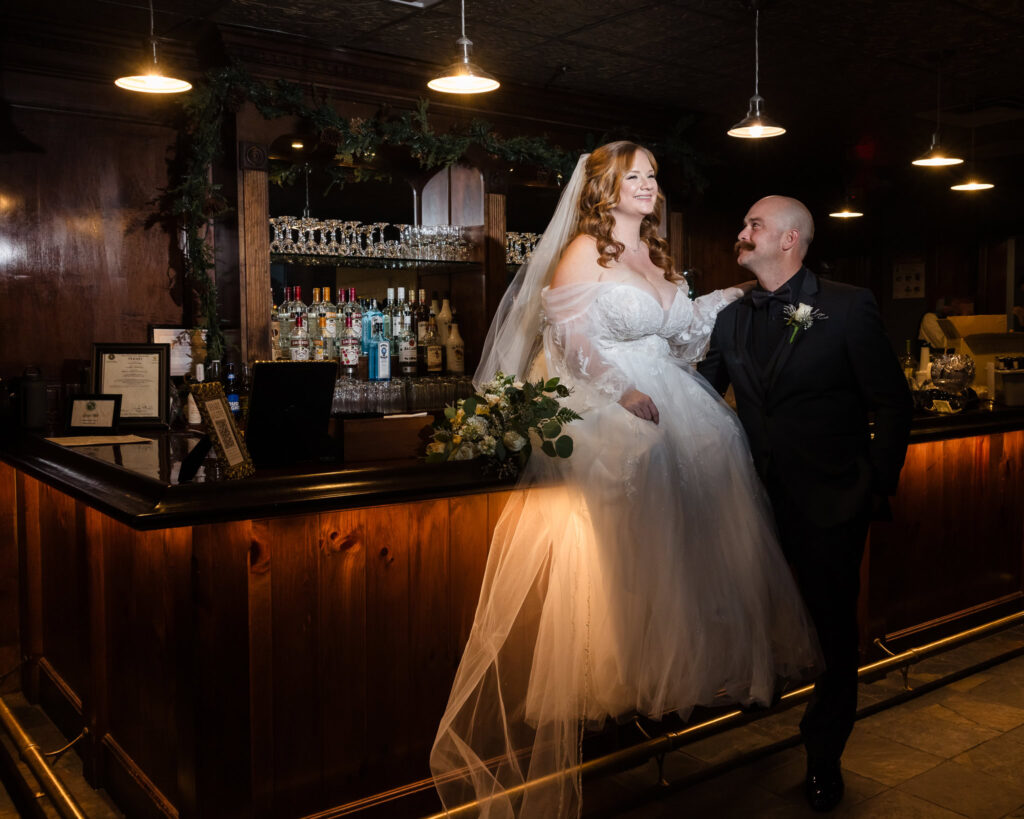 Bride and groom posing playfully in the wood-paneled bar room, a perfect mix of elegance and personality.