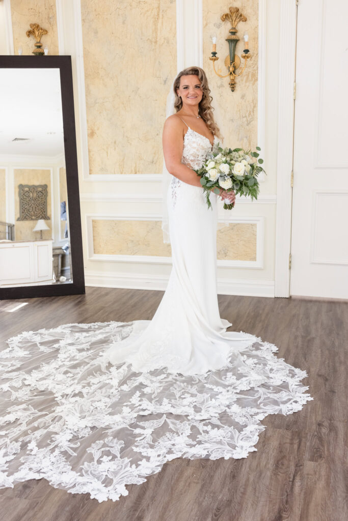 Full-length bridal portrait showcasing an intricate lace train and elegant bouquet, captured in the light-filled bridal suite at Stonebridge Country Club.