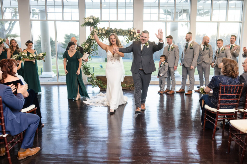 Newlyweds joyfully walk down the aisle as husband and wife at Stonebridge Country Club, arms raised in celebration as guests cheer around them.
