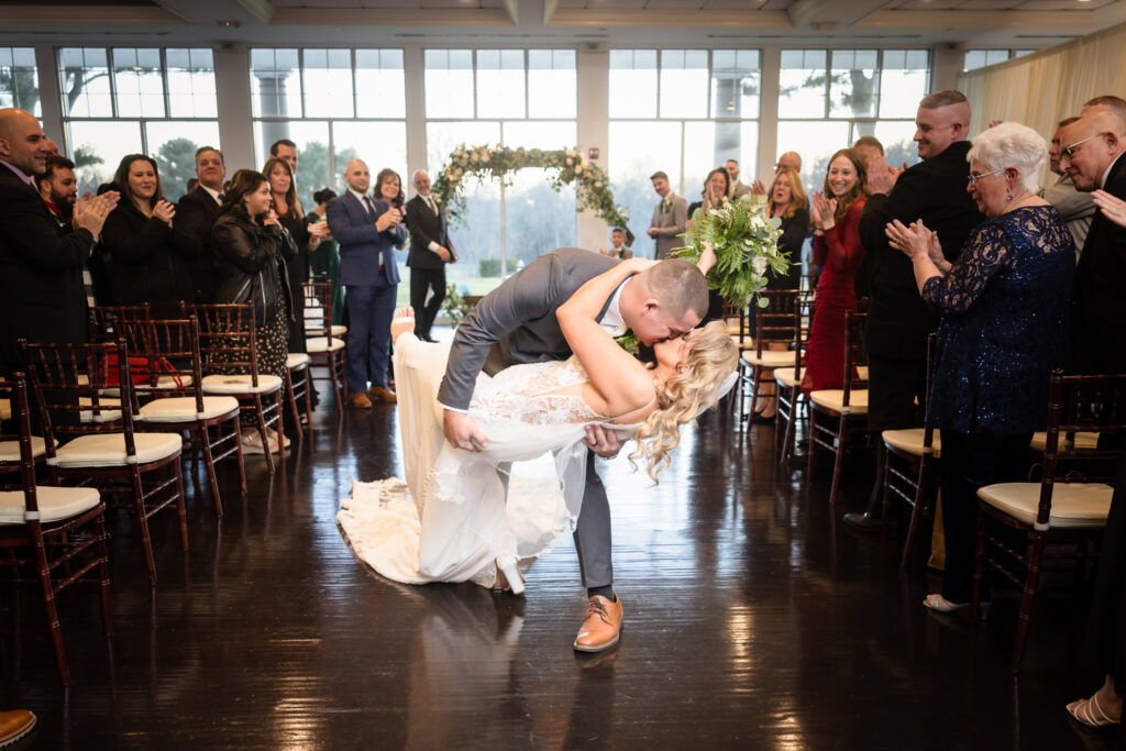 Groom dips the bride for a romantic kiss in the center aisle as guests applaud their grand exit at Stonebridge Country Club.


