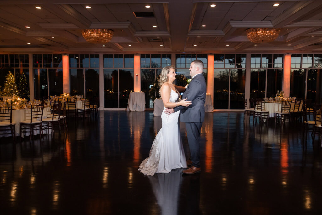 Bride and groom share their first dance in the grand ballroom at Stonebridge Country Club, surrounded by warm uplighting and glowing twilight reflections.

