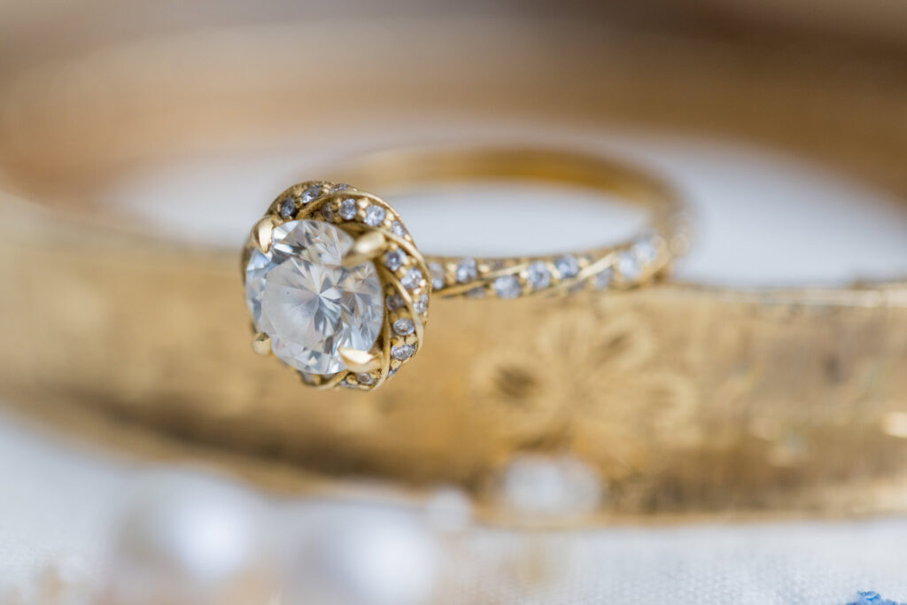 Close-up of a gold engagement ring with a brilliant-cut diamond, nestled among heirloom jewelry pieces and soft pearls.

