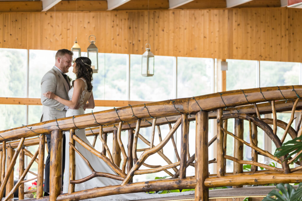 Newlyweds share an intimate moment atop Flowerfield’s wooden bridge, surrounded by warm wood tones and greenery in the indoor botanical atrium.

