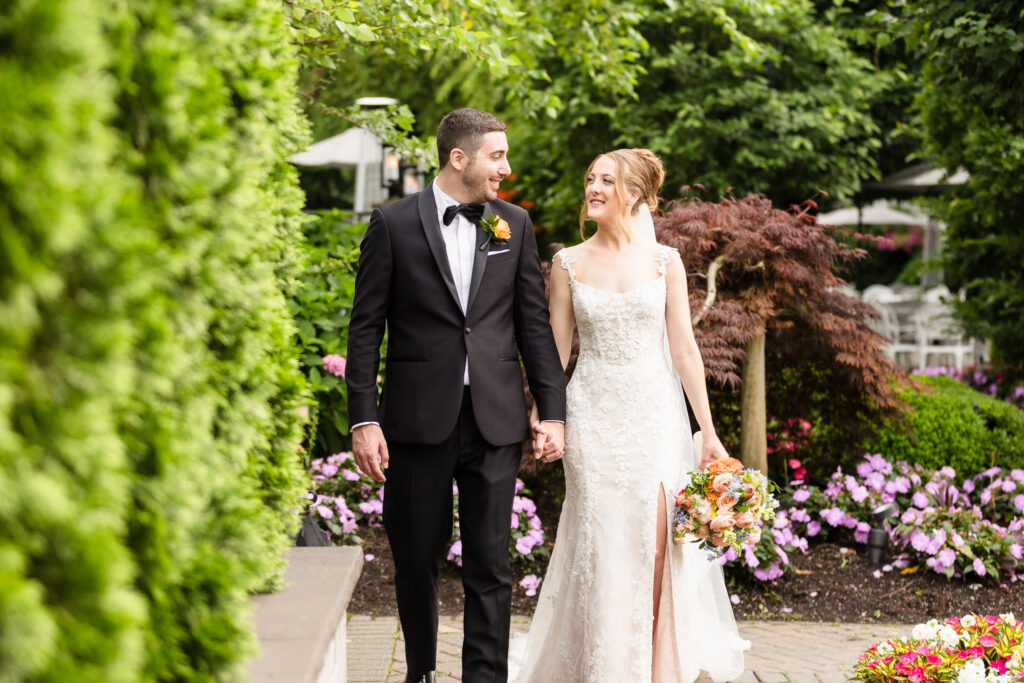 Newlyweds walking hand in hand through the lush gardens at Watermill Caterers during their wedding portraits.