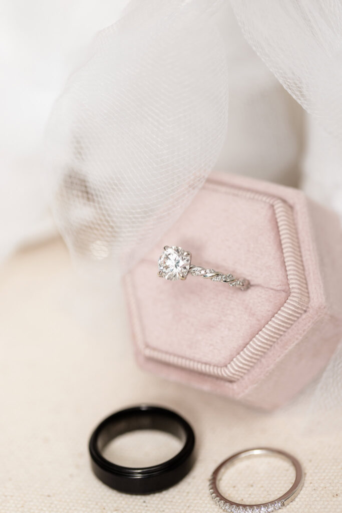 Elegant flat lay of wedding rings and blush velvet ring box on soft white linen