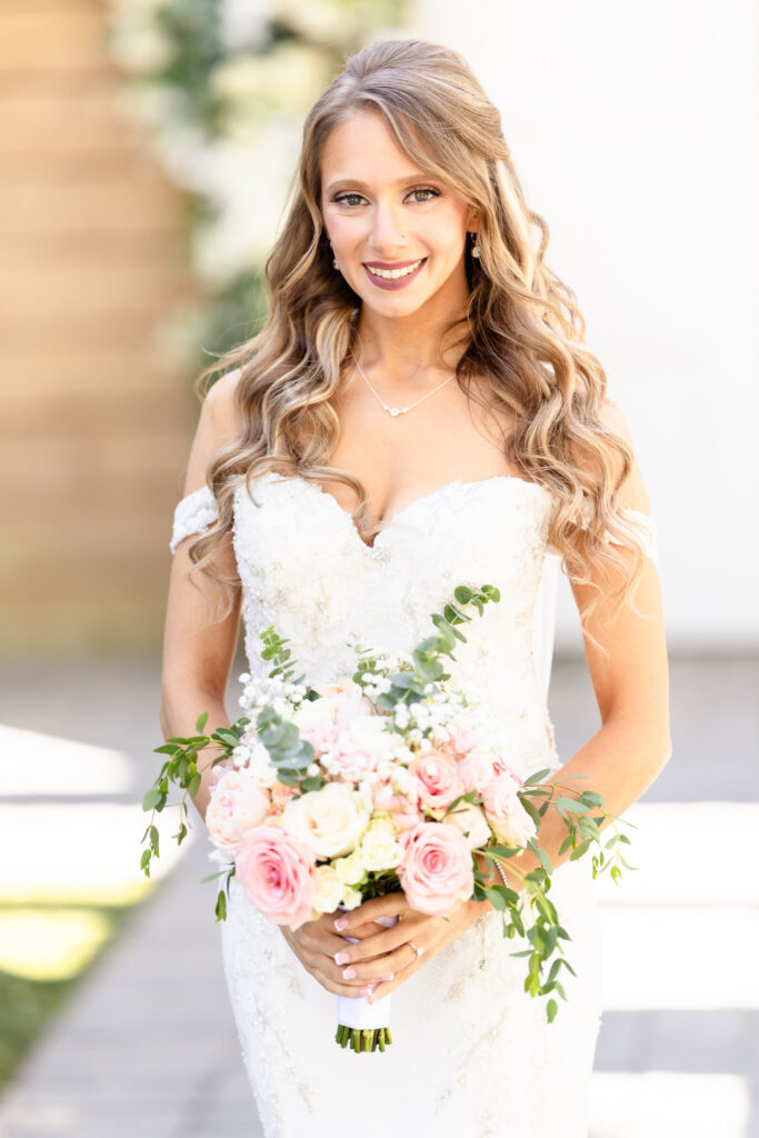 Bride smiling while holding her bouquet in soft sunlight
