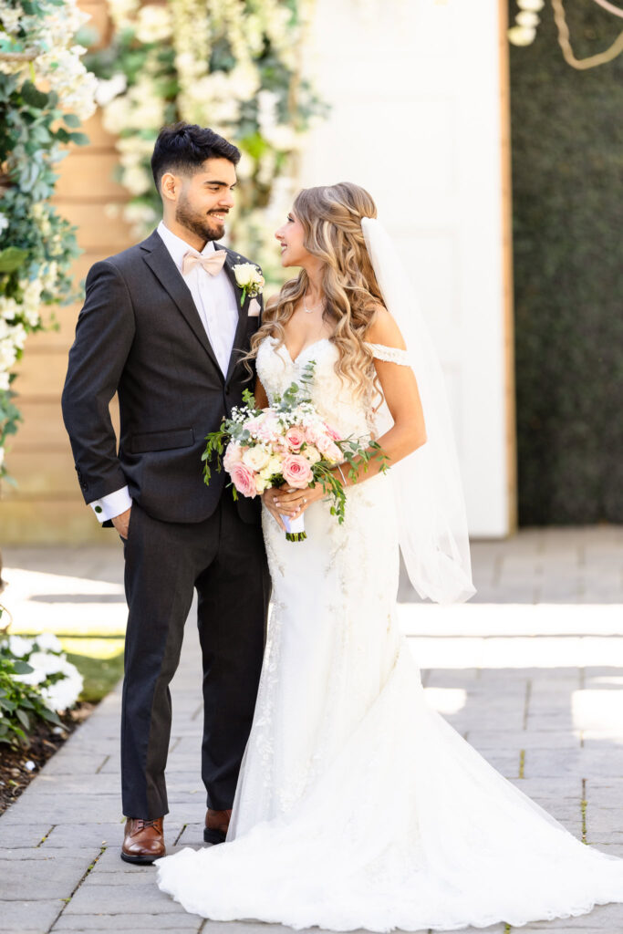 Bride and groom standing together in front of ceremony floral arch