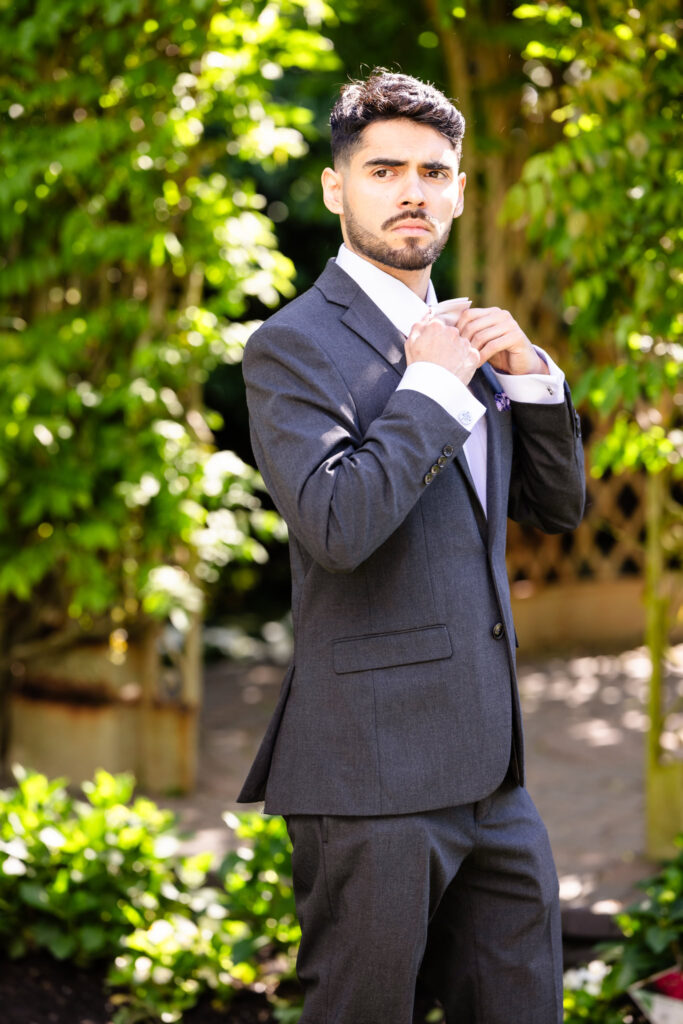 Groom adjusting cufflinks outdoors in a classic black suit