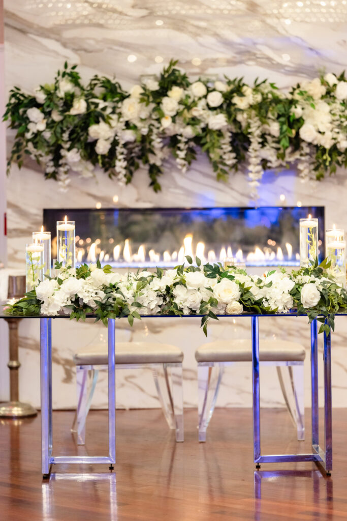 Candlelit head table under suspended florals in the Watermill’s reception space.