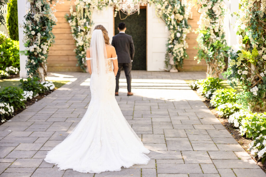 Bride walking toward the groom for a private first look in the garden courtyard at Watermill Caterers.